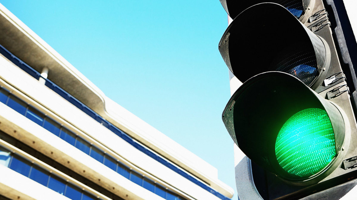 Traffic Light with Green Light Lit up in Foreground Right, Office Building in Background Left